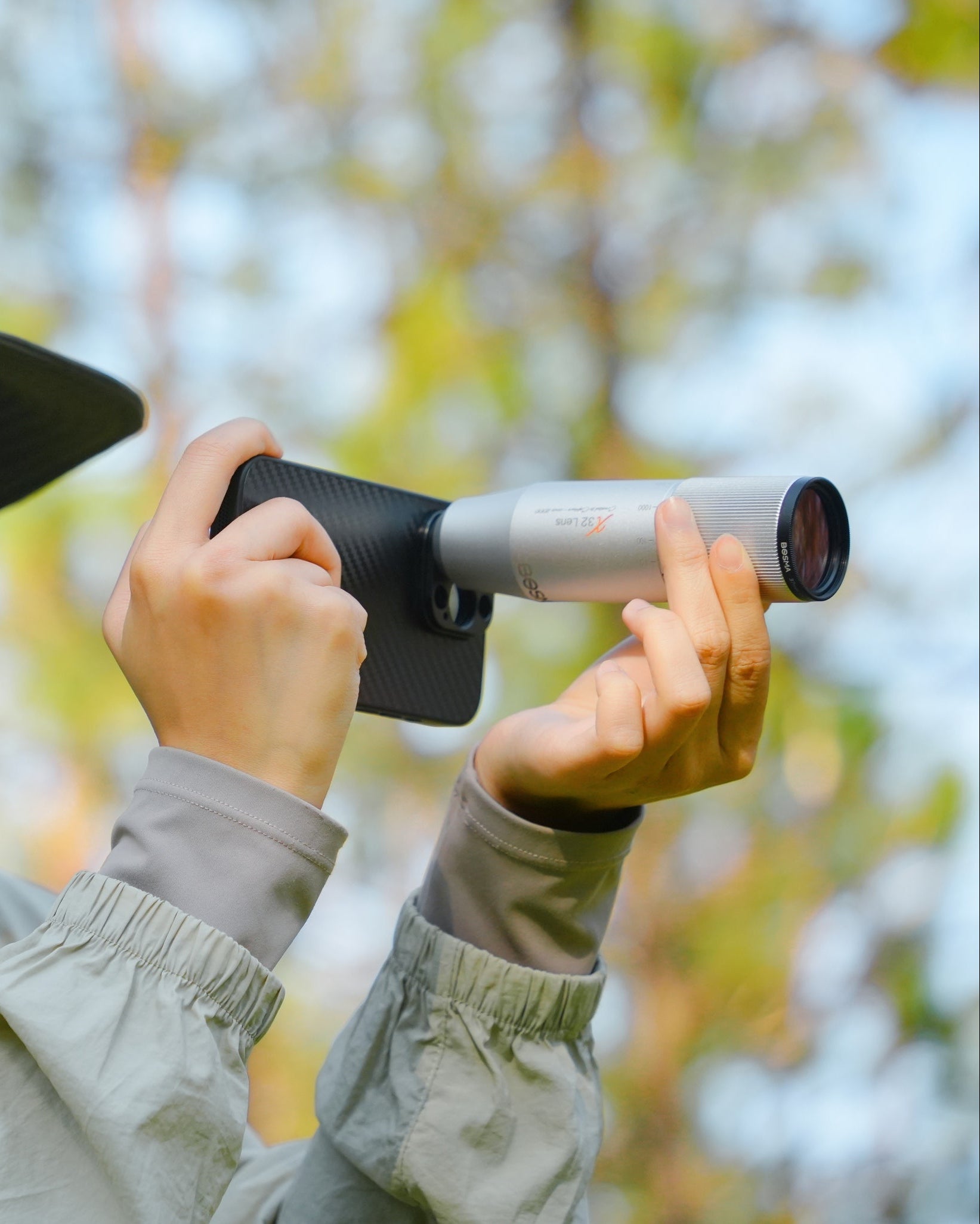 Person in outdoor gear holding a bosma telephoto phone lens with a mobile for birding photography and videography